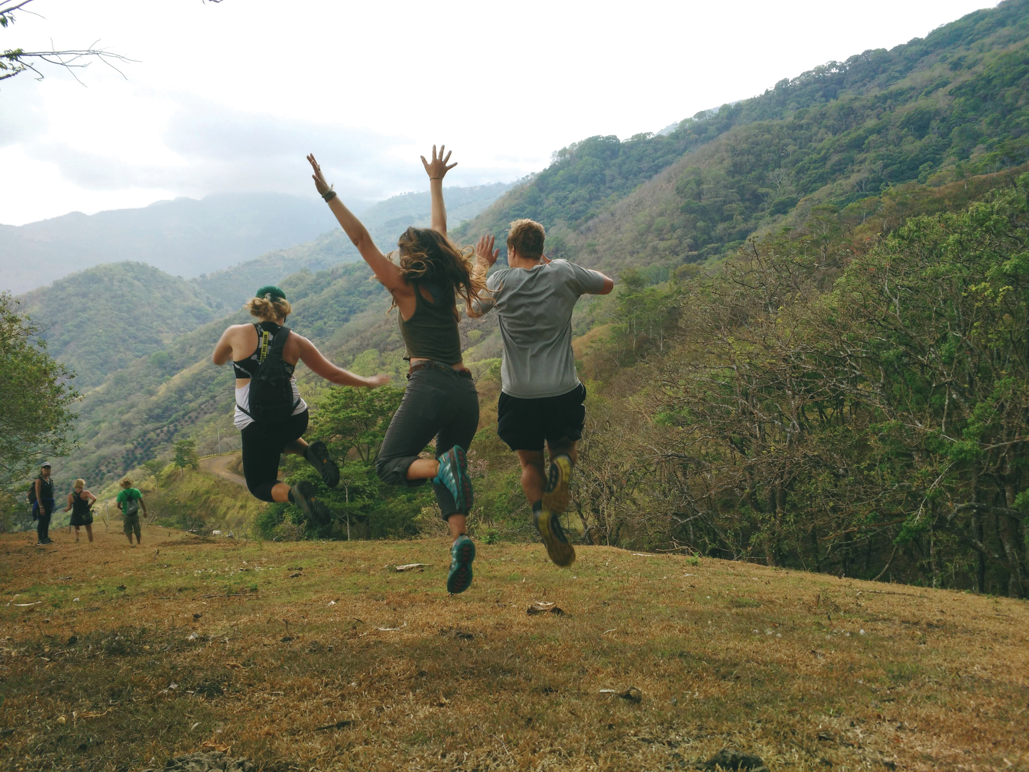 A group of students run and jump across the green hills of a Costa Rican countryside.