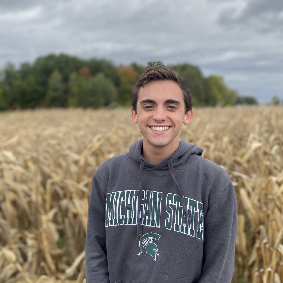 Image of a young man with dark hair standing in a field wearing a Spartan hoodie.